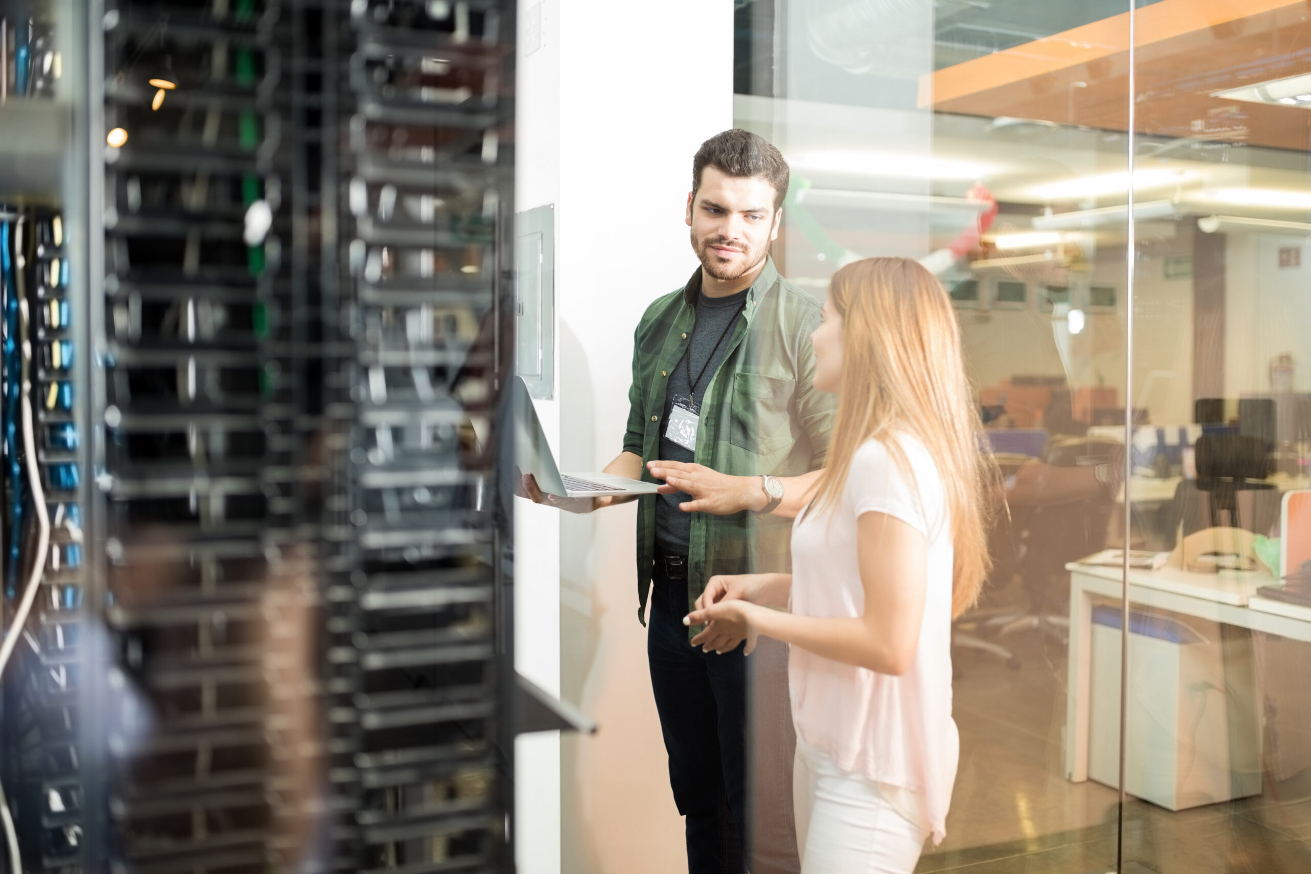 IT technician holding laptop and client discuss within server room