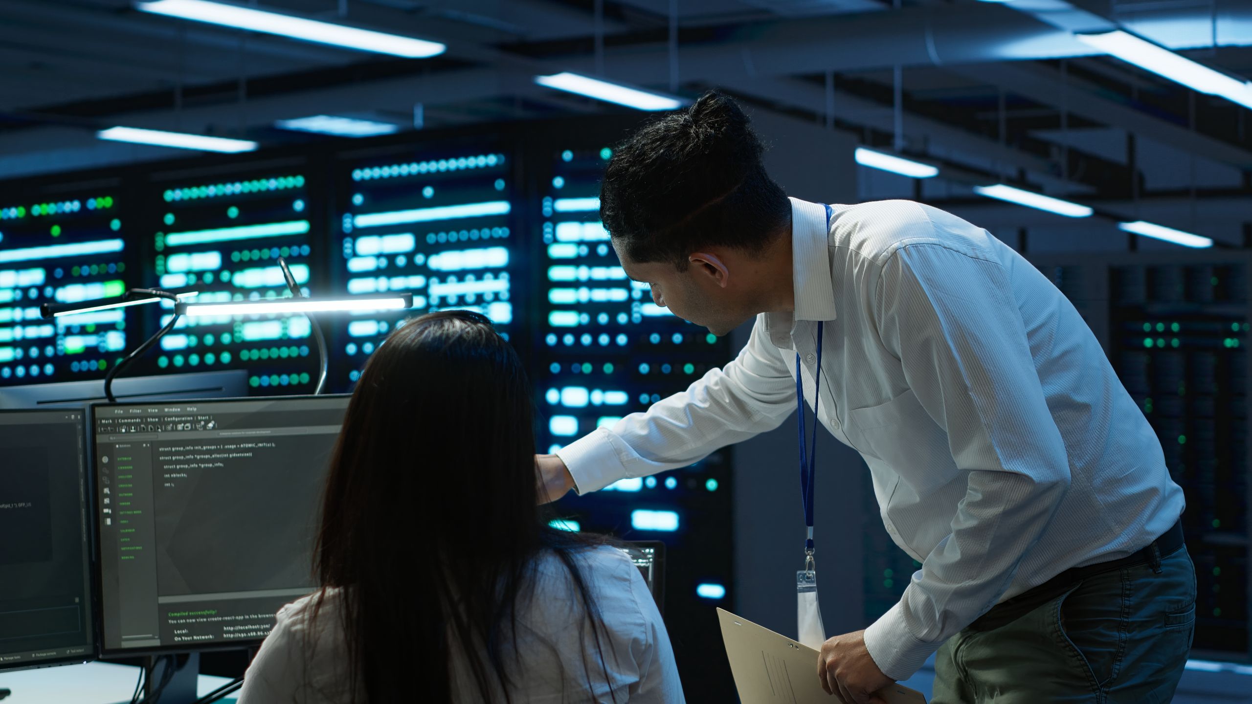 Engineer pointing at monitor beside colleague inside data center.