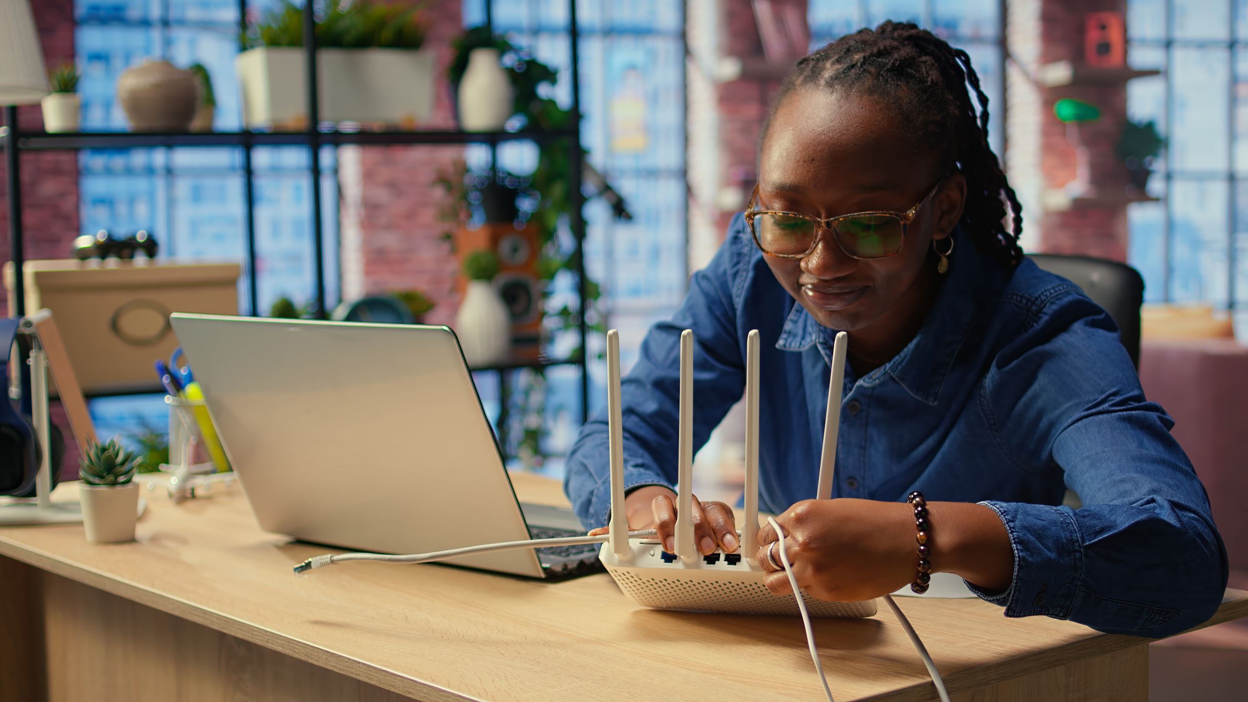 Woman connecting cables to Wi-Fi router beside laptop.